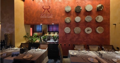Restaurant dining area with a red textured wall displaying circular art plates and a 'Don Juan' sign, tables set with glasses, plates, and napkins.