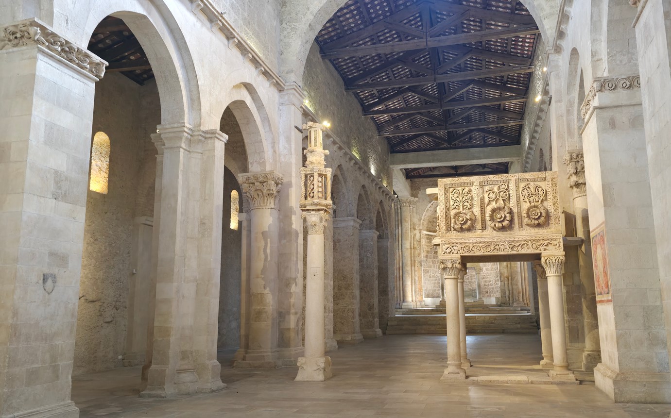 Interior of a stone cathedral hall with tall arches and carved columns, featuring a decorative stone screen on the right.