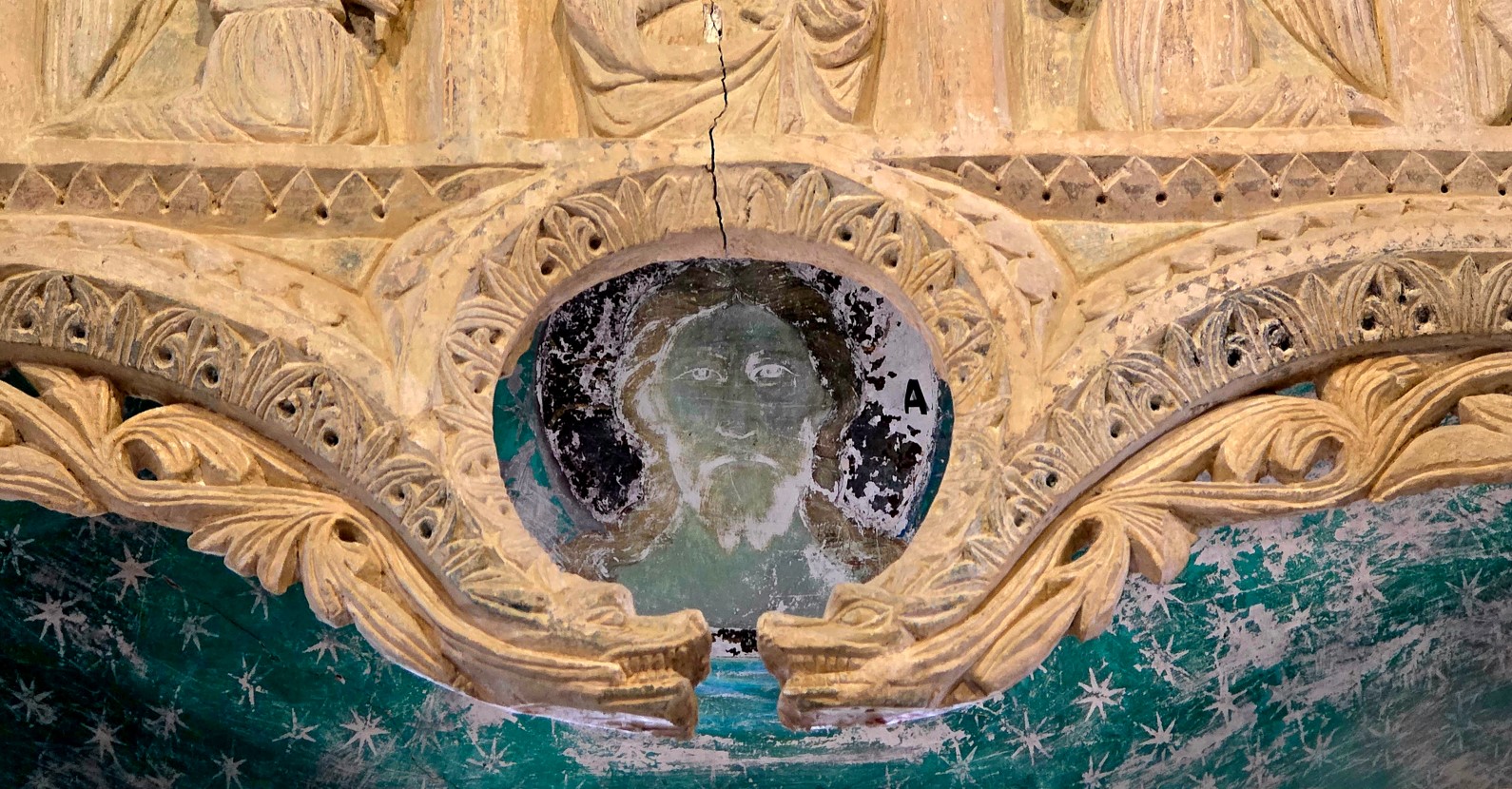 Circular carved medallion with a faint bearded face, surrounded by ornate laurel-like foliage in weathered stone.