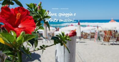 Bright beach club scene with a red hibiscus in the foreground, lounge chairs and umbrellas on the sand, blue sea in the background; overlay reads 'Mare, spiaggia e infinite emozioni…'