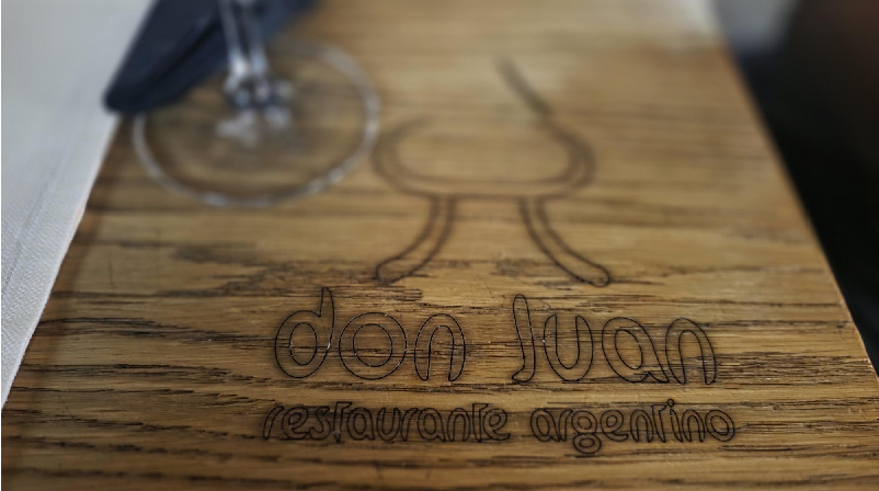 Wooden sign for Don Juan Restaurante Argentino with a wine glass illustration.