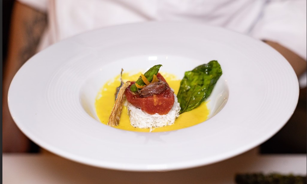 Menu_zero_sprechi | Food and Wine Magazine Elegant plated appetizer: a small stack of white cheese topped with tomato tartare, microgreens, and shaved carrot on a yellow sauce.