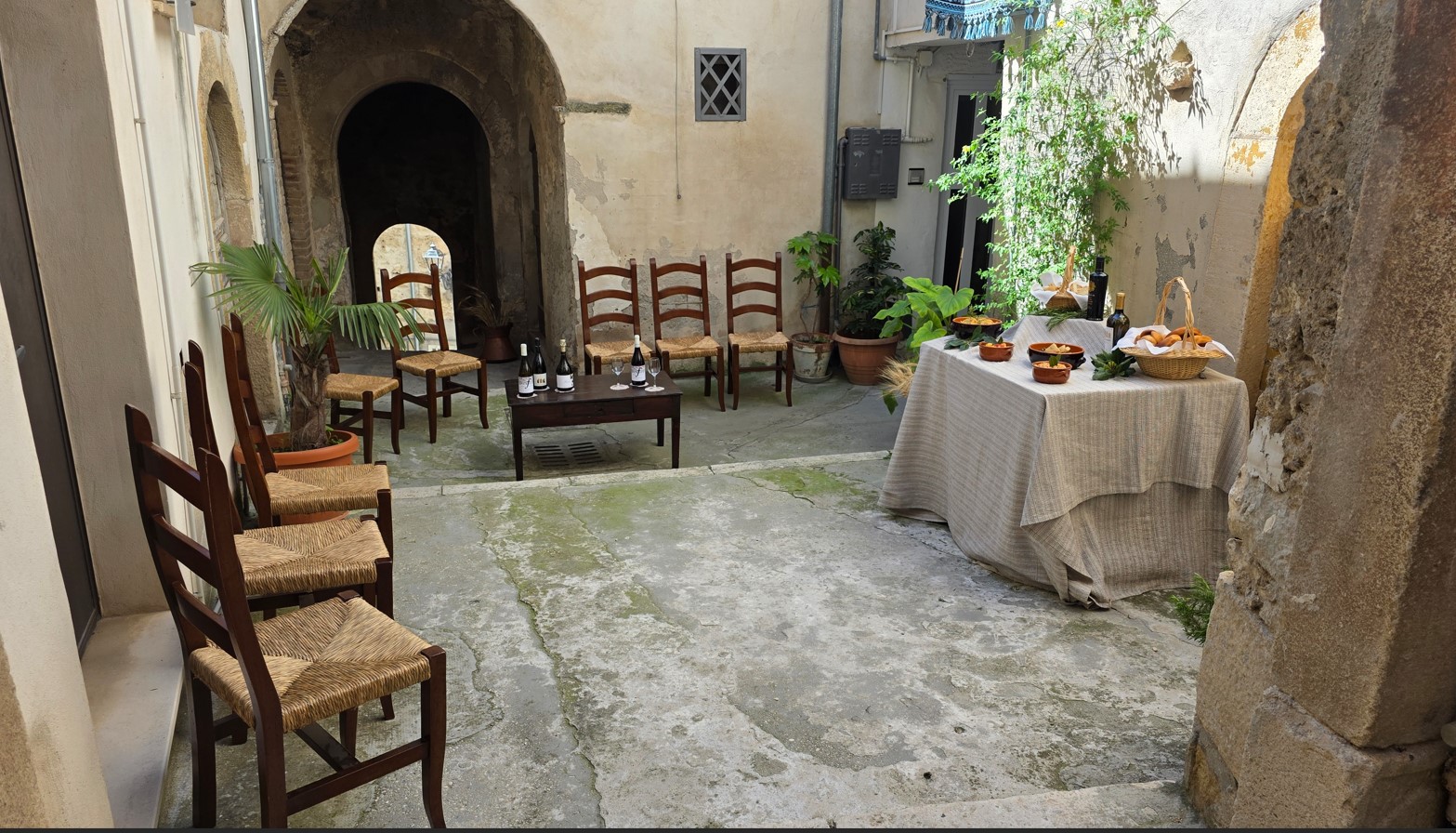 Stone courtyard set for a small gathering: wooden chairs arranged around a low table with wine bottles and glasses.