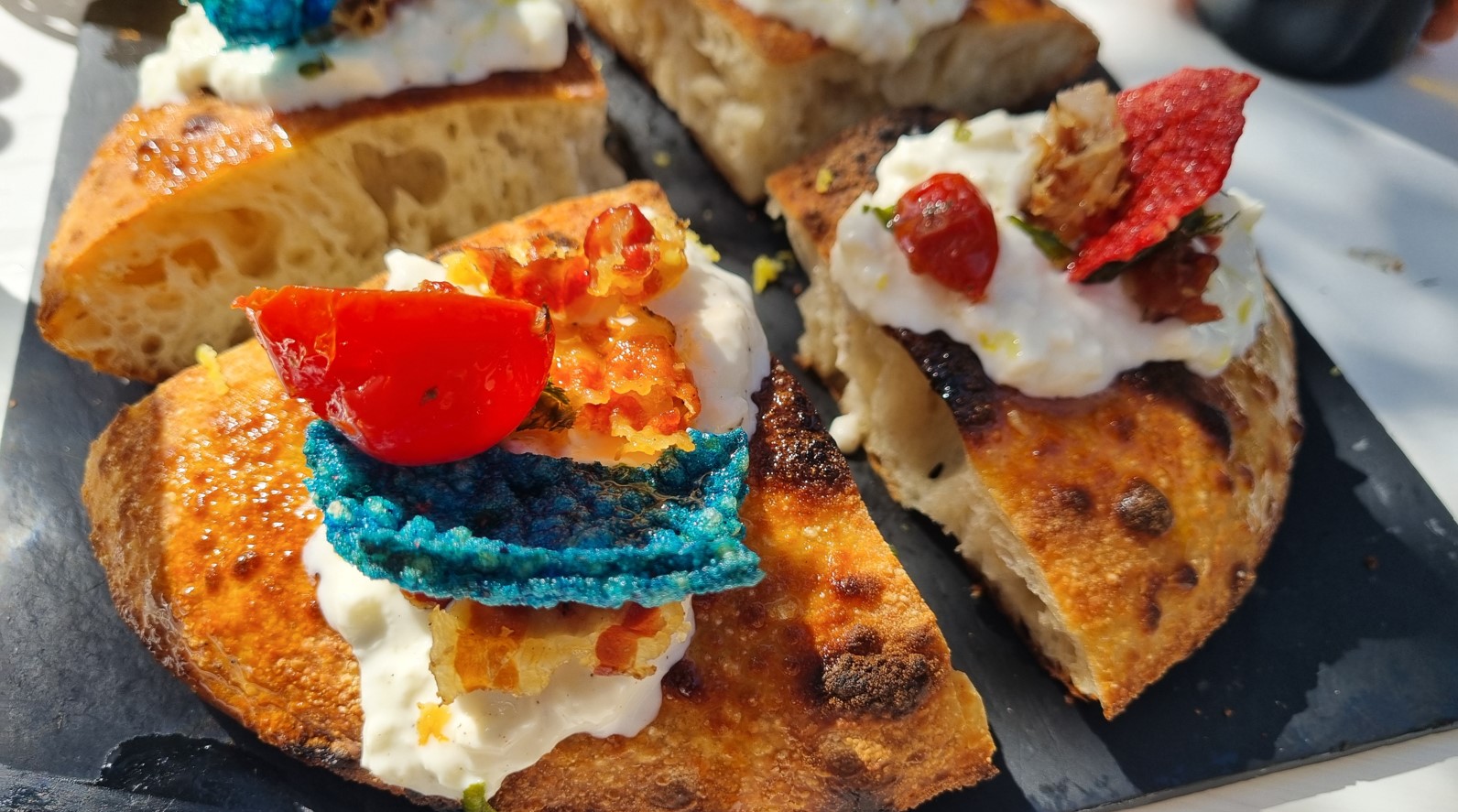 Pizza_cilentana | Food and Wine Magazine Crostini platter with toasted baguette slices topped for tasting: cream cheese, red pepper pieces, and a blue tortilla chip garnish on a slate board