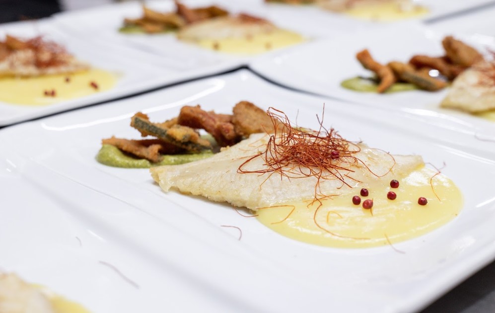 Poseidonia_cilento_menu_zero_sprechi | Food and Wine Magazine Plated white fish fillet on yellow sauce with saffron threads, red peppercorns, and a side of crispy garnish on a white plate of a fine-dining dish.