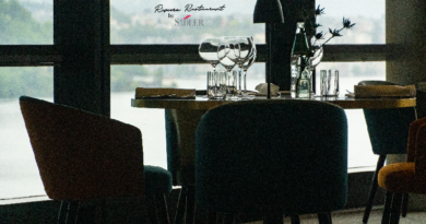Round dining table set for a meal in a modern restaurant, with wine glasses, water glasses, and a small vase by a large window.
