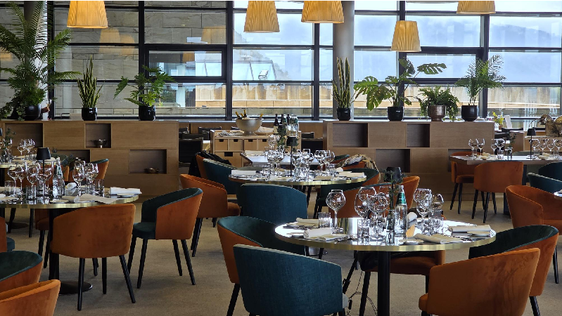 Rivierarestaurant_interni | Food and Wine Magazine Round tables set for dining in a modern restaurant, with wine glasses, plates, and cutlery ready for guests.