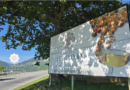Roadside billboard advertising Tenuta Secolo IX winery with a glass of white wine and grape clusters, set against trees and hills in the background.
