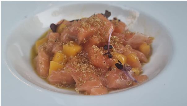 Cantina Della Vetra_tartare Salmone | Food and Wine Magazine Plate of diced pink fish with mango chunks, microgreens, and a light citrusy crumble on top; restaurant-style presentation in a shallow bowl.
