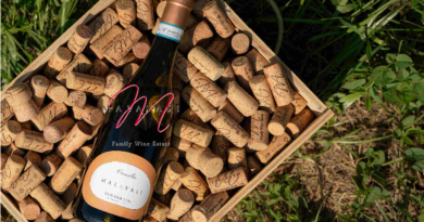 Wine bottle in a wooden crate filled with corks, outdoors on grass; label reads 'Family Wine Estate'