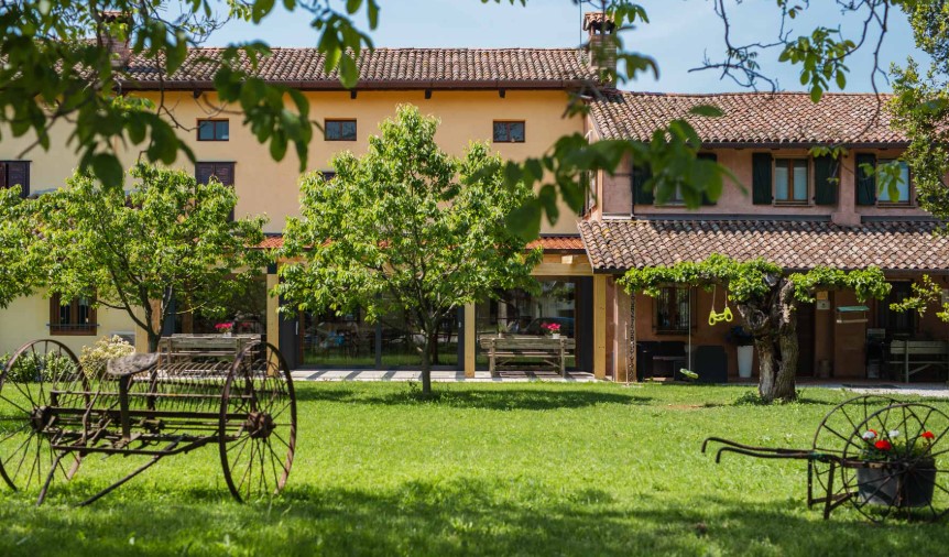 Rustic yellow building with a red-tiled roof, front lawn, and trees; old wagon wheels sit in the grass in the foreground.