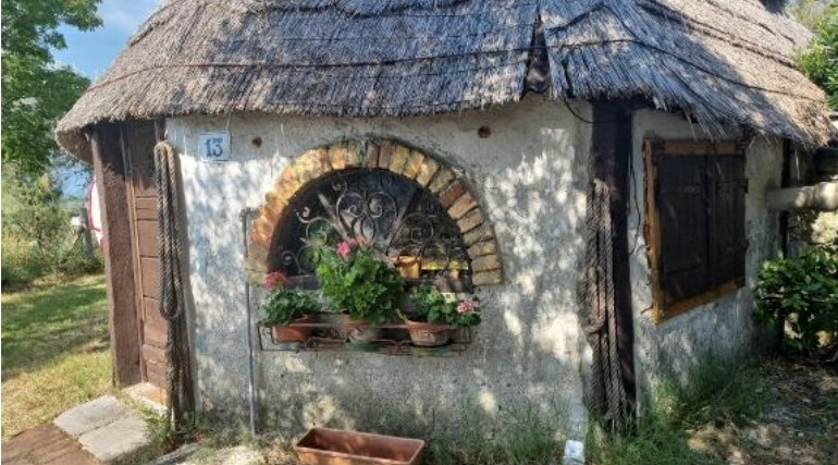 Small rustic cottage with a thatched roof and arched window filled with potted flowers on a garden wall