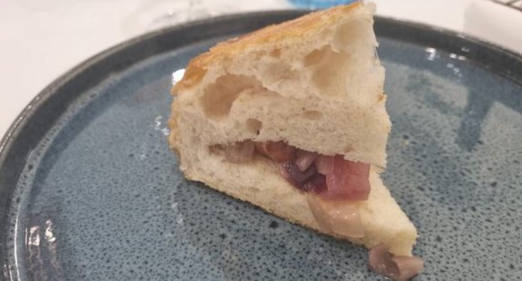 La Ciacolada_pizza_cotta_al_vapore | Food and Wine Magazine Triangular wedge of crusty white bread filled with sautéed onions and mushrooms on a blue plate behind.