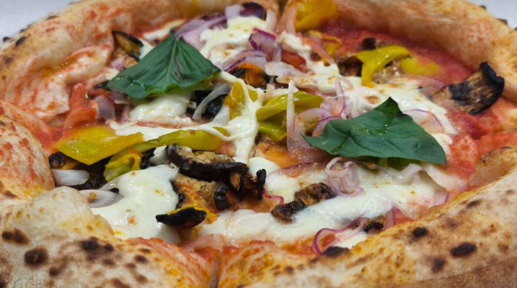Pizza topped with melted cheese, tomato sauce, yellow pepper, red onion, mushrooms, and fresh basil leaves