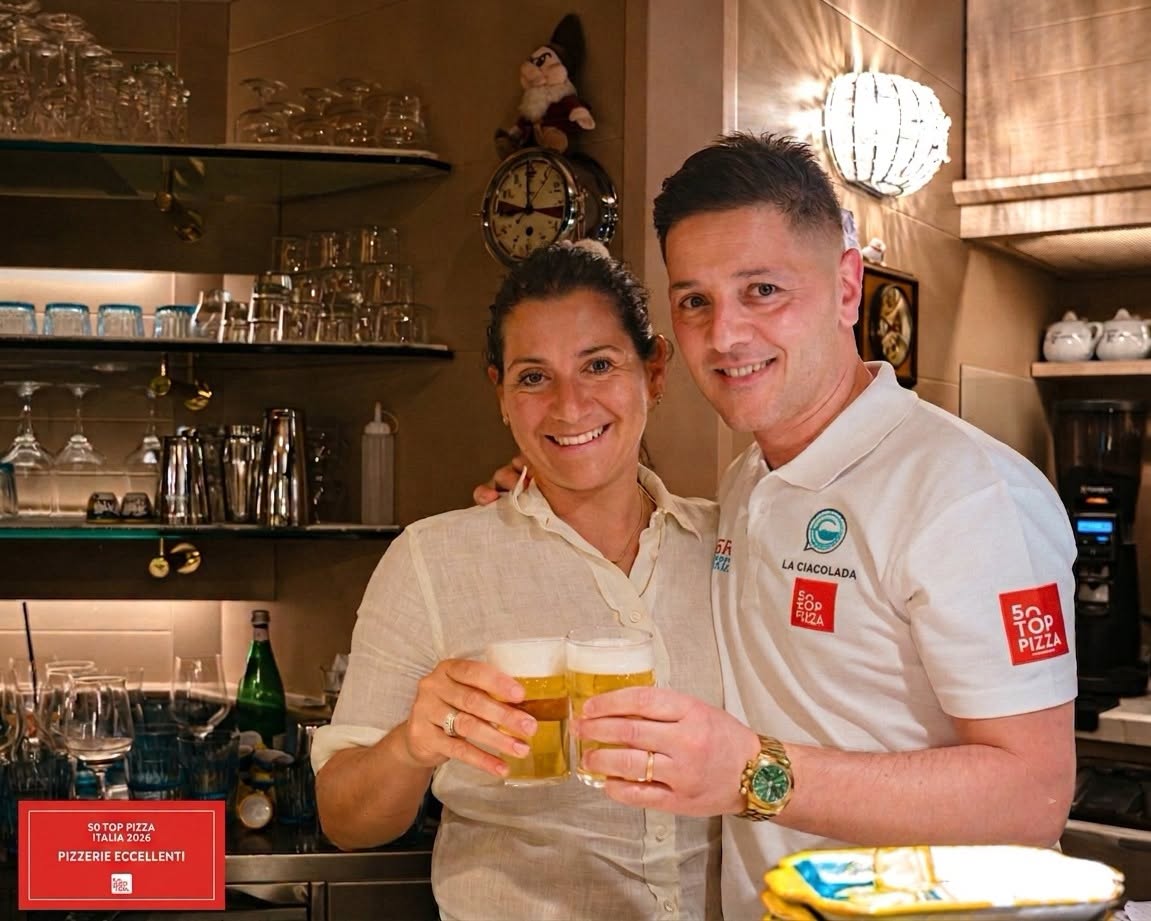 Laura E Luigi | Food and Wine Magazine Smiling man and woman toast with beer glasses behind a bar area.